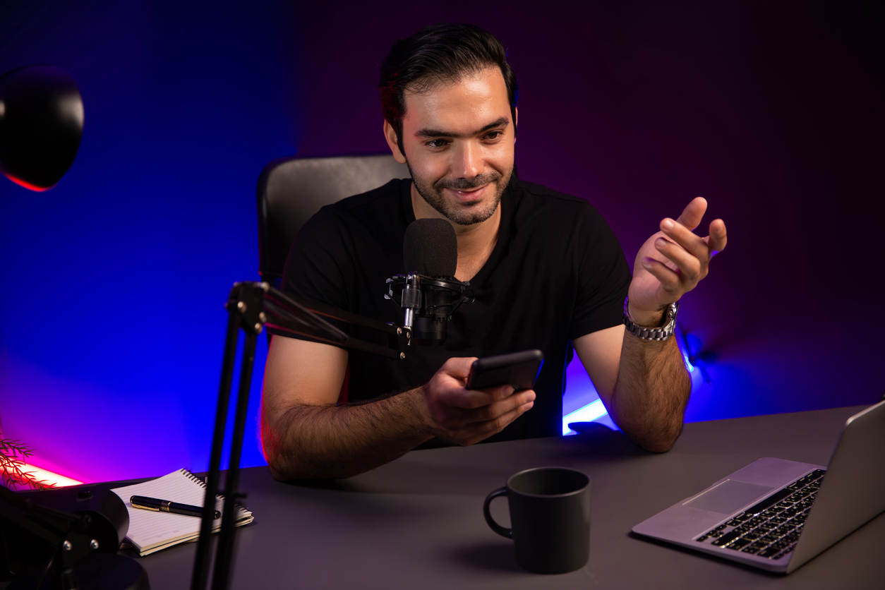 Content creator recording a video at a desk with a microphone, laptop, and phone