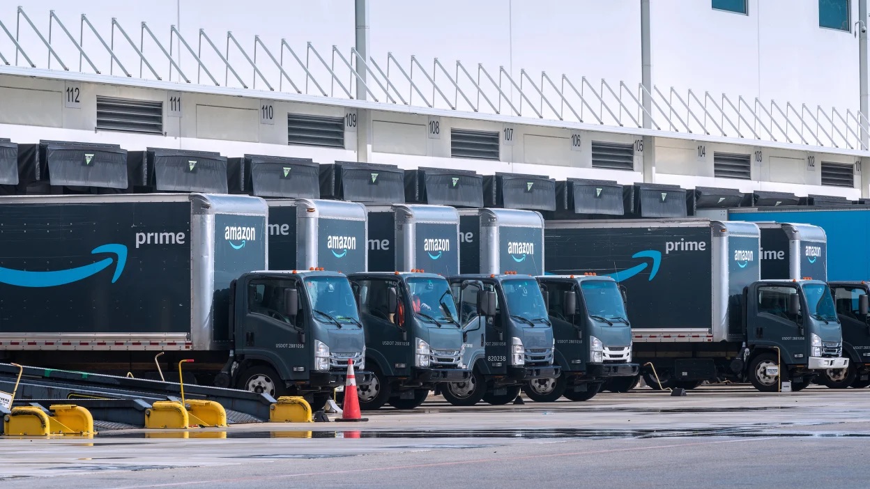 Row of Amazon Prime delivery trucks parked at a fulfillment center loading dock